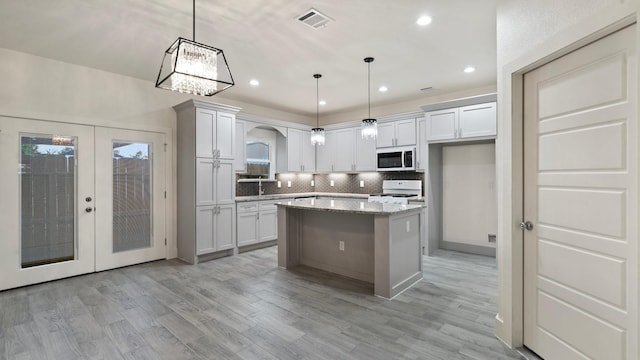 kitchen with french doors, light stone countertops, a center island, and decorative light fixtures