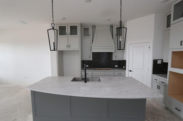 kitchen featuring light stone counters, custom range hood, a sink, unfinished concrete floors, and stovetop