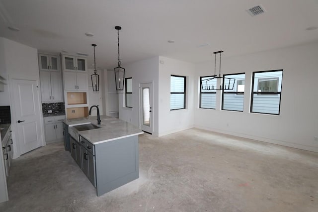 kitchen featuring tasteful backsplash, visible vents, unfinished concrete flooring, decorative light fixtures, and a sink