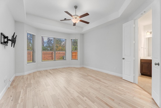 spare room with ceiling fan, light wood-type flooring, and a tray ceiling