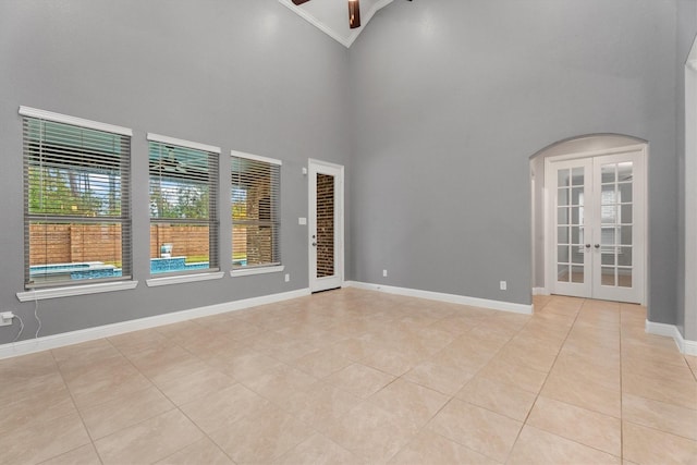 tiled spare room with ceiling fan, a high ceiling, and french doors