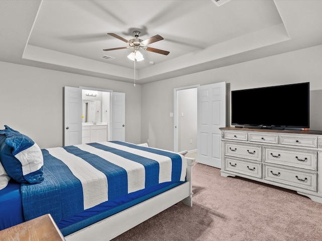 carpeted bedroom featuring a raised ceiling, ensuite bath, and ceiling fan