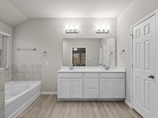 bathroom with vanity, wood-type flooring, a tub, and vaulted ceiling