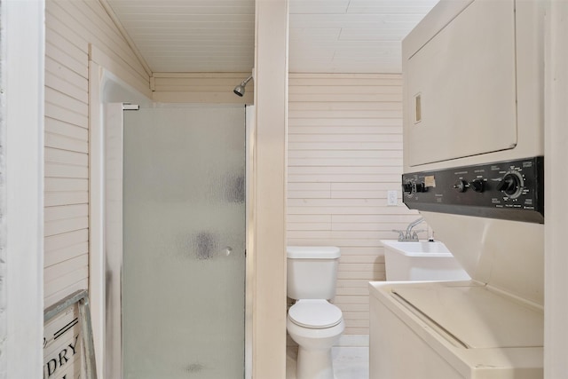 bathroom featuring toilet, stacked washing maching and dryer, a shower with door, and wooden walls