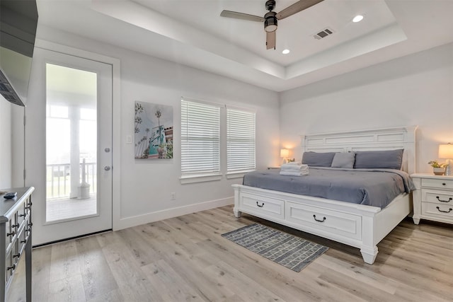 bedroom featuring ceiling fan, access to exterior, light wood-type flooring, and a tray ceiling