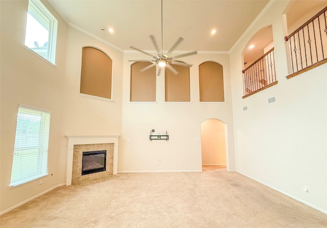 unfurnished living room featuring a tile fireplace, ceiling fan, a high ceiling, crown molding, and light carpet