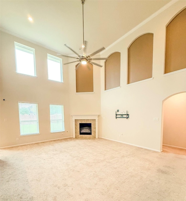 unfurnished living room with a towering ceiling, carpet floors, ceiling fan, and ornamental molding