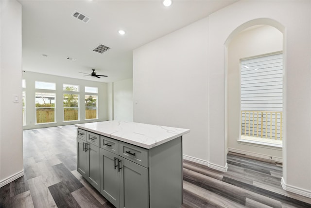 kitchen with gray cabinetry, a center island, ceiling fan, light stone countertops, and dark hardwood / wood-style flooring