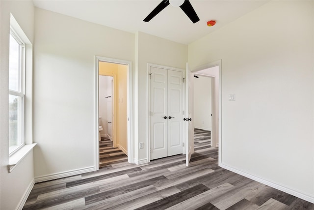 unfurnished bedroom featuring wood-type flooring, a closet, ensuite bath, and ceiling fan