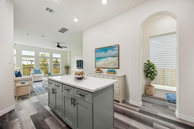 kitchen with light stone countertops, gray cabinetry, ceiling fan, a center island, and dark hardwood / wood-style floors