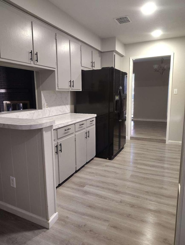 kitchen with light hardwood / wood-style floors, black fridge with ice dispenser, kitchen peninsula, and a chandelier