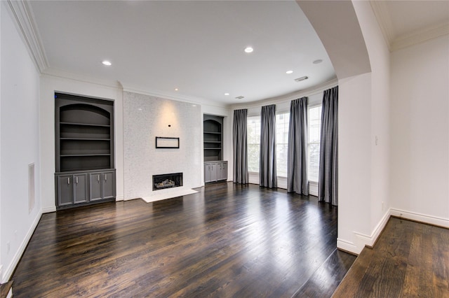 unfurnished living room featuring a fireplace, built in shelves, dark wood-type flooring, and crown molding