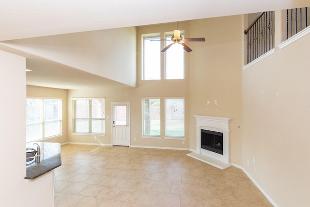 unfurnished living room with ceiling fan, light tile patterned flooring, and a high ceiling