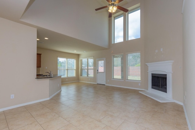 unfurnished living room featuring light tile patterned floors, sink, ceiling fan, and a high ceiling