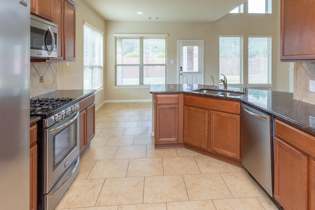 kitchen featuring sink, stainless steel appliances, dark stone countertops, decorative backsplash, and light tile patterned flooring