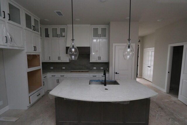 kitchen featuring cooktop, sink, pendant lighting, a center island with sink, and white cabinets