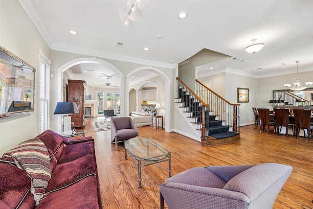 living room with ceiling fan with notable chandelier, light hardwood / wood-style floors, and crown molding