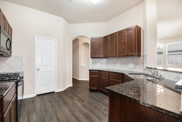 kitchen featuring backsplash, sink, dark hardwood / wood-style floors, dark stone countertops, and black gas range oven