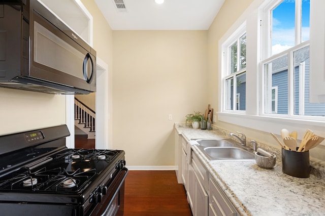 kitchen with light stone countertops, sink, dark wood-type flooring, black gas range oven, and dark brown cabinets