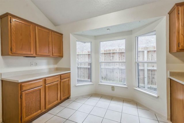 kitchen with a textured ceiling, light tile patterned floors, and vaulted ceiling