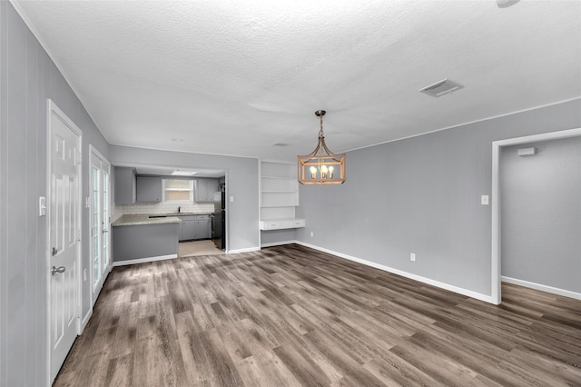 unfurnished living room featuring dark hardwood / wood-style floors, a textured ceiling, and an inviting chandelier