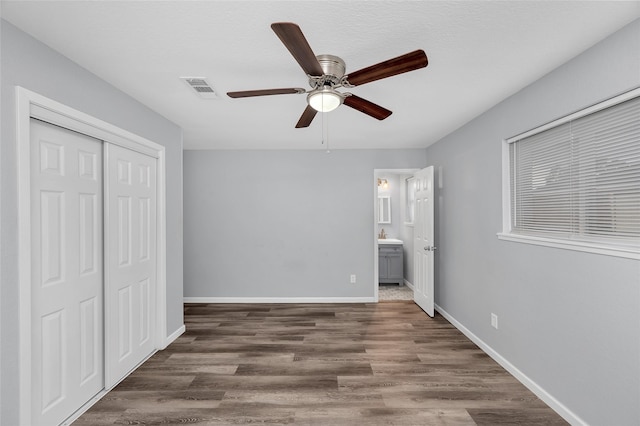 unfurnished bedroom featuring ceiling fan, dark hardwood / wood-style flooring, connected bathroom, and a closet