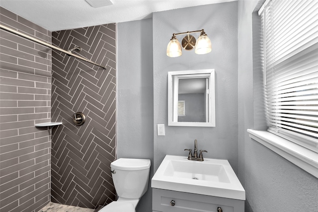 bathroom with a textured ceiling, vanity, toilet, and tiled shower