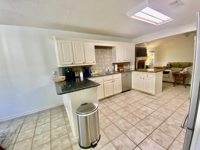 kitchen with kitchen peninsula, sink, stainless steel dishwasher, tasteful backsplash, and white cabinetry