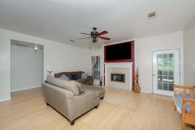 living room featuring ceiling fan, light wood-type flooring, and a tile fireplace