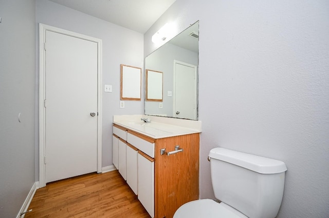 half bathroom with baseboards, vanity, toilet, and wood finished floors