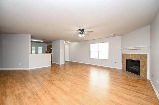 unfurnished living room featuring baseboards, ceiling fan, light wood finished floors, and a tiled fireplace