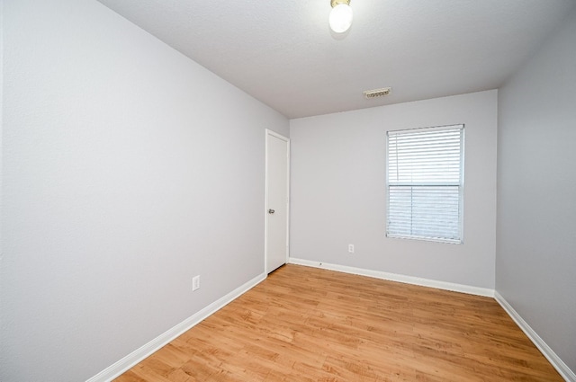 empty room featuring baseboards, visible vents, a textured ceiling, and light wood finished floors