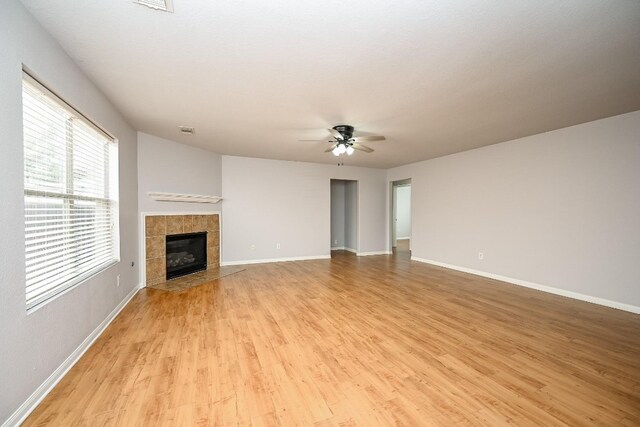 unfurnished living room featuring baseboards, a tiled fireplace, a ceiling fan, and light wood-style floors