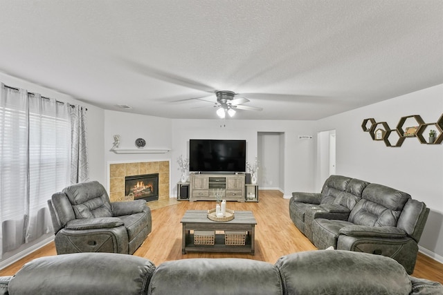 living room with wood-type flooring, ceiling fan, a textured ceiling, and a fireplace