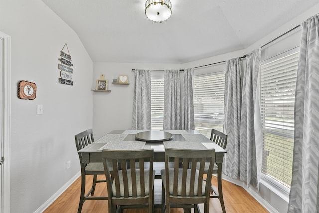 dining room with vaulted ceiling, light wood-style flooring, and baseboards