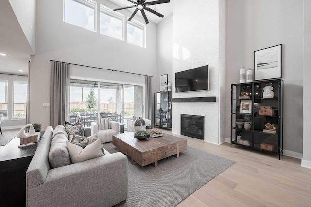 living room featuring light hardwood / wood-style floors, a healthy amount of sunlight, a towering ceiling, and a tile fireplace