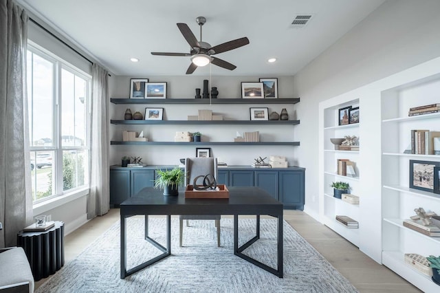 office space featuring hardwood / wood-style floors, built in shelves, a healthy amount of sunlight, and ceiling fan