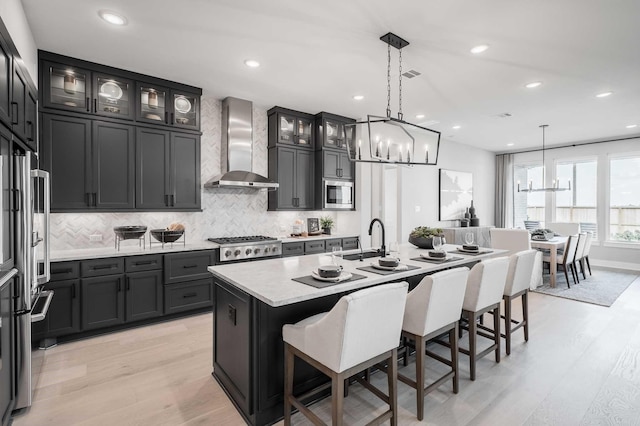 kitchen featuring a center island with sink, wall chimney exhaust hood, light hardwood / wood-style flooring, and appliances with stainless steel finishes