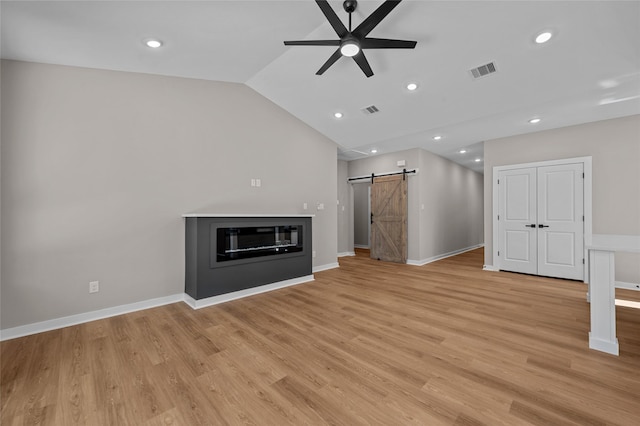 unfurnished living room featuring a barn door, ceiling fan, light hardwood / wood-style floors, and lofted ceiling