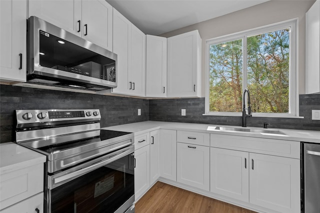 kitchen with appliances with stainless steel finishes, backsplash, sink, light hardwood / wood-style flooring, and white cabinets