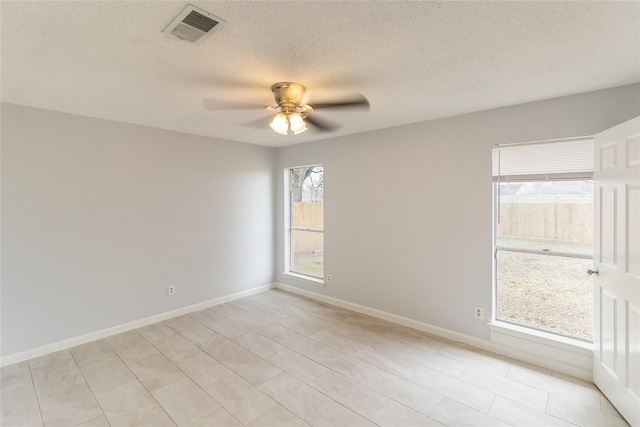 tiled empty room featuring a wealth of natural light, ceiling fan, and a textured ceiling