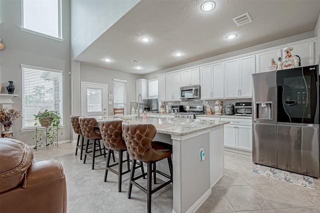 kitchen featuring white cabinetry, a breakfast bar area, stainless steel appliances, a kitchen island with sink, and light tile patterned flooring