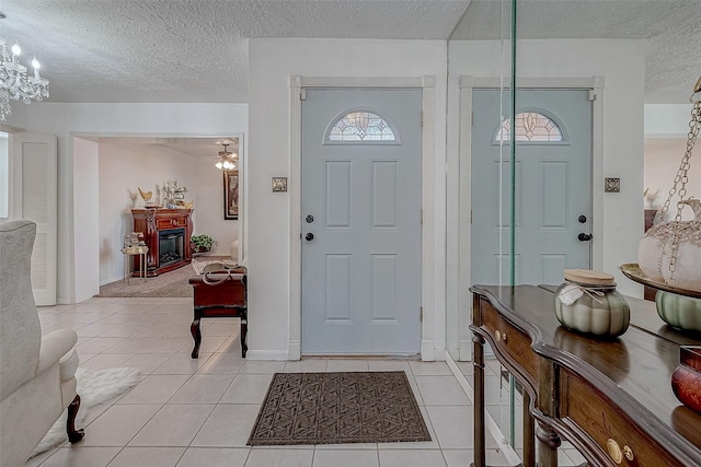 entrance foyer featuring ceiling fan with notable chandelier, light tile patterned floors, and a textured ceiling