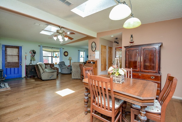 dining area with a textured ceiling, a skylight, light hardwood / wood-style flooring, and ceiling fan