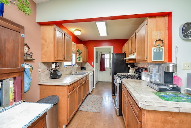 kitchen featuring white dishwasher, sink, light hardwood / wood-style flooring, stainless steel gas stove, and decorative backsplash