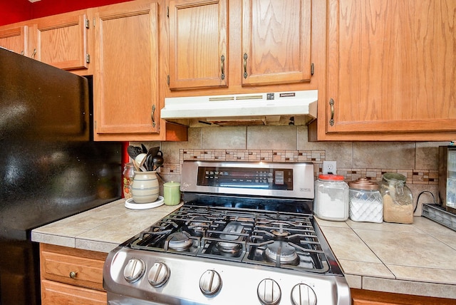 kitchen featuring tile countertops, decorative backsplash, gas stove, and black refrigerator