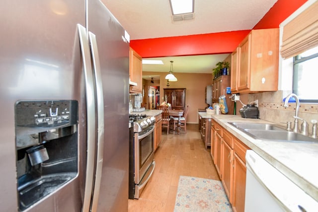 kitchen featuring sink, light hardwood / wood-style flooring, decorative backsplash, decorative light fixtures, and stainless steel appliances