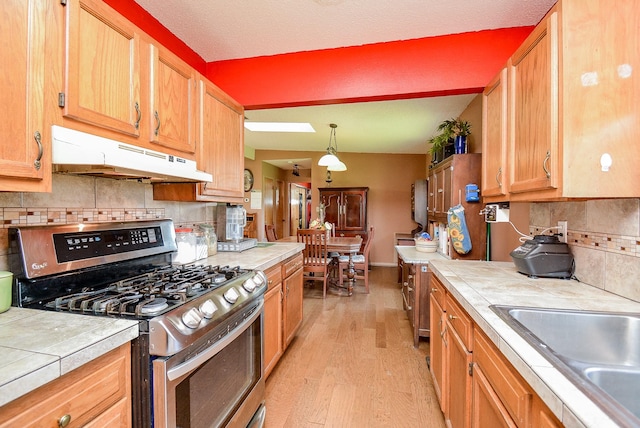 kitchen featuring light wood-type flooring, stainless steel gas stove, tile countertops, and backsplash