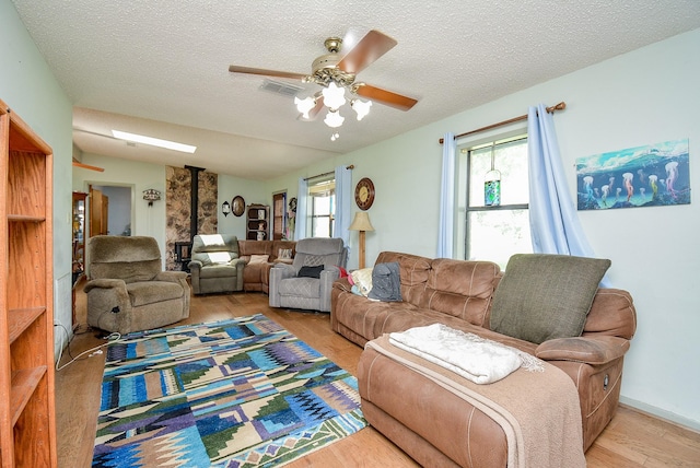 living room with a textured ceiling, light hardwood / wood-style flooring, a wood stove, and ceiling fan