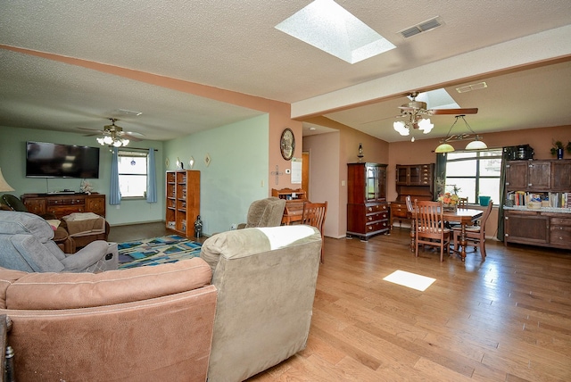 living room with a skylight, a textured ceiling, hardwood / wood-style flooring, and ceiling fan